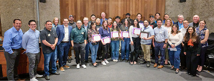 Group of students holding certificates surrounded by faculty and partners