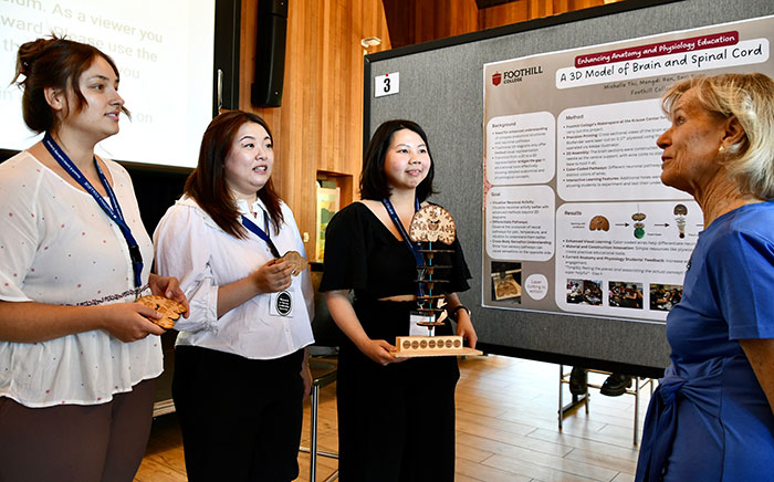 three female students holding a spinal cord model and talking with an instructor