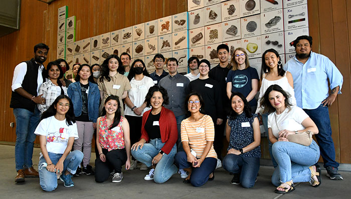 Group of about 30 students standing in front of periodical table of elements mural