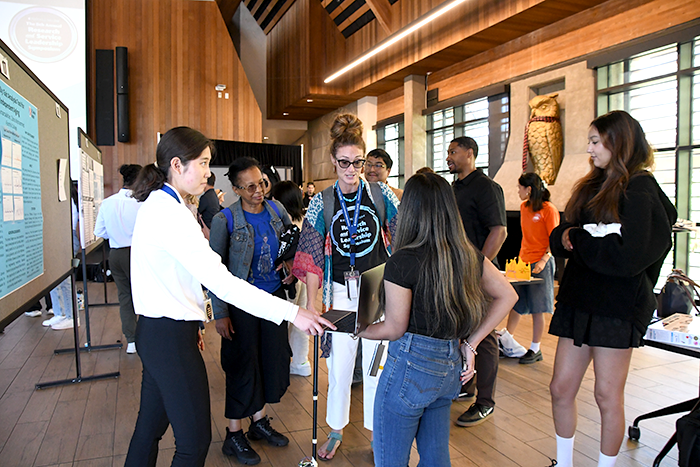 crowd around two students presenting at symposium in large hall